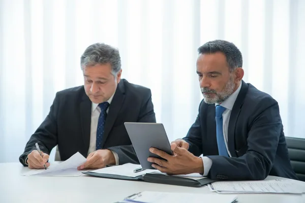 Two professionals in suits reviewing tax documents at conference table